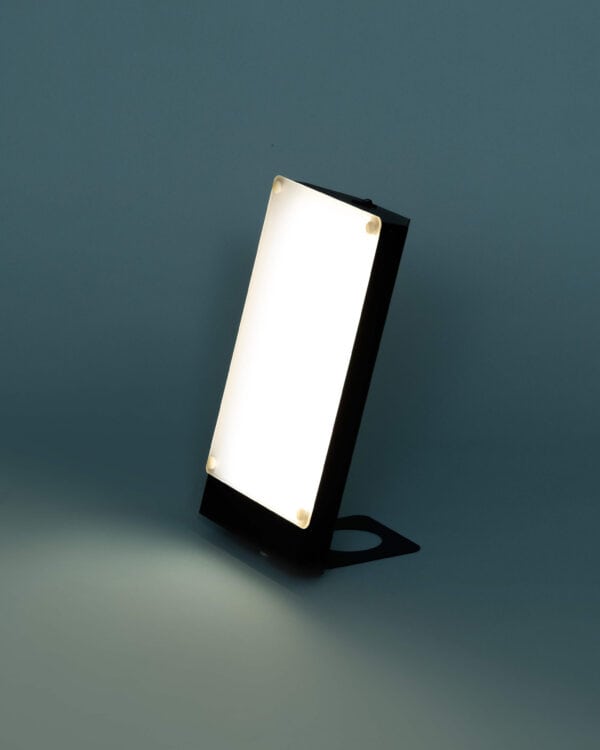 TRAVelite Desk Lamp II side view in black lit on a turquoise background