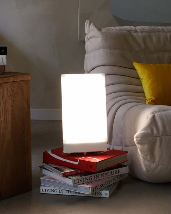 TRAVelite Desk Lamp II lit sitting on top of a pile of books on the floor